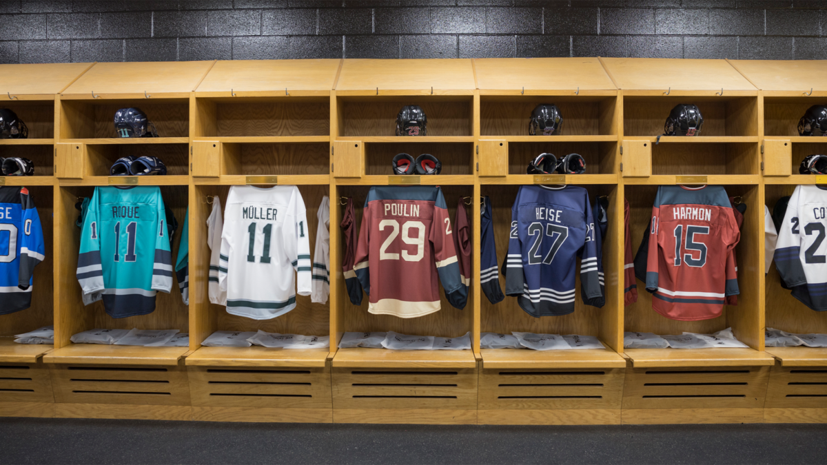 PWHL jersey designs hanging in stalls. From left to right: Nurse #20, Roque #11, Muller #11, Poulin #29, Heise #27, Harmon #15, and Coyne's jersey cut out of frame.